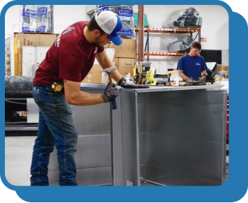 a technician in a red shirt holding a hammer works on a piece of equipment in a warehouse