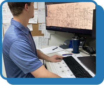 a man in a blue polo sits at a computer desk and looks at a screen